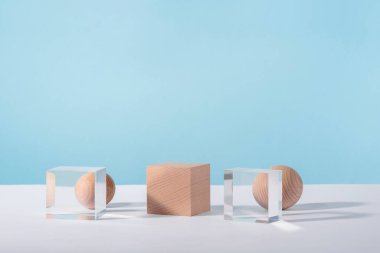 Yaratıcı geometrik ürün sahnesi, kozmetik ekran platformu, ürün reklamcılığı, geometrik duruş. Ahşap ve cam küp kürsü, kozmetik veya mücevher için mavi zemin üzerinde küre