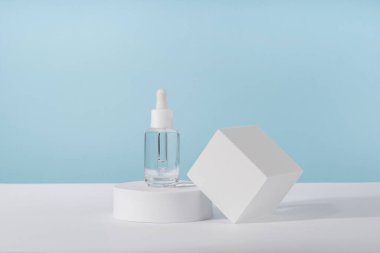 Serum kozmetik şişesi, peptit ve retinol ile mavi arka planda platform kaidesi. Yağ kozmetik şeffaf moda ürünleri ambalajı. Serum güzellik düşürücü model
