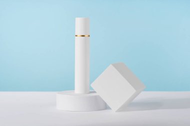 Maket kürsünün mavi arka planında kozmetik lüks krema şişesi maketi. Markasız losyon güzellik ürünü ambalajı. Ürün sunumu taklit ediliyor. Losyon, cilt temizleyicisi.