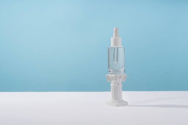 Hyaluronik asit kozmetik ürünleri şık malzemelerle paketleme yapıyor. Serum kozmetik şişesi, peptit ve retinol ile mavi arka planda podyum kaidesi. Serum güzellik düşürücü model