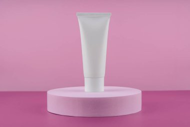 Beyaz kozmetik ürünü tüp pembe arka planda podyum kaidesi üzerinde. Krem şişesi, losyon, cilt bakımı için krem şanti. Güzellik temizleyicisi, şampuan standı. Güneş kremi sunum modeli