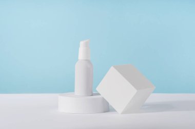 Beyaz geometrik kaide podyumunda mavi arka planda kozmetik krem metalik pompa modeli. Markasız losyon güzellik ürünü ambalajı. Ürün sunumu maketi