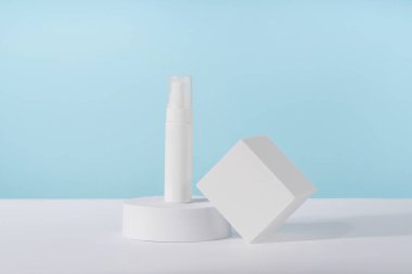 Maket kürsünün mavi arka planında kozmetik krem şişesi maketi. Markasız losyon güzellik ürünü ambalajı. Ürün sunumu taklit ediliyor. Losyon, köpük, temizleyici, cilt bakımı için şampuan.