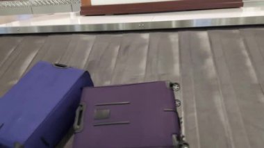 Varış bölgesindeki bagaj taşıma bandında çeşitli bavullar hareket ediyor.