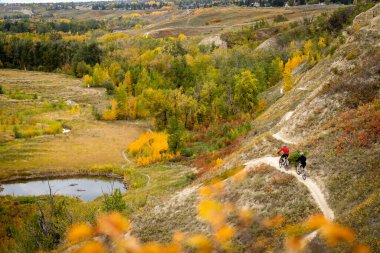 Two mountain bikers ride the Bowmont trail system in autumn colours above Dale Hodges Park in Calgary Alberta Canada clipart