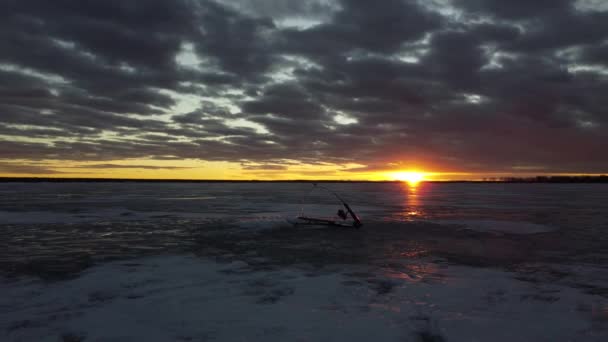 カナダ北部の凍結氷に光の反射と日没のシーンでの氷釣りロッドの周りの空中追跡運動 — ストック動画