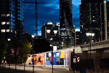 Calgary Alberta Canada, 11 Eylül 2022: Uzak bir inşaat vinci, Telus binası ve Bridge Caddesi duvar resimleri ile East Village bölgesinin akşam fotoğrafı.