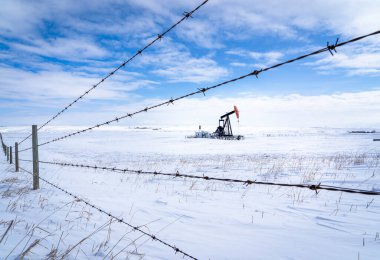 Rocky View County Alberta Canada 'da Kanada çitleri üzerinde karla kaplı bir tarımsal alanda çalışan bir petrol pompası krikosu..