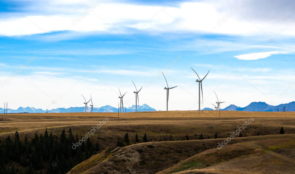 Wind turbines standing tall generating electricity with the Canadian Rocky Mountains at background near Pincher Creek Alberta Canada.