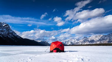 Kananaskis İl Parkı Alberta 'daki Kanadalı Rocky Dağları' nda donmuş bir gölde dimdik duran alabalık avlamak için buzda balık avlama çadırı..