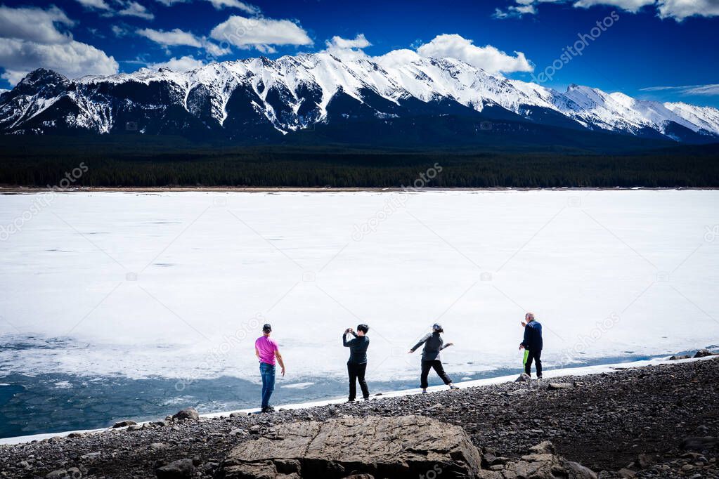 Tourists taking pictures along the lakeshore of Lower Kananaskis Lake with the Canadian Rockies at background.