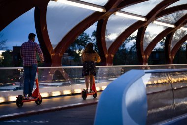 Calgary Alberta Canada, 16 Mayıs 2022: Akşamüstü saatlerinde popüler bir şehir merkezinde, Barış Köprüsü 'nden e-scooterla geçen iki kişi.
