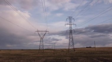 Elektrik hatlarının altındaki hava ters izleme hareketi ve Alberta bozkırlarında tozlu çakıllı bir yoldan geçen bir araba ile iletim kuleleri..