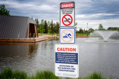 Airdrie Alberta Canada, 12 Haziran 2022: Nose Creek Parkı 'ndaki ahşap bir sahil yolu boyunca kamu amfi tiyatrosu yakınlarındaki bir alabalık havuzunda uyarı levhası sergilendi.