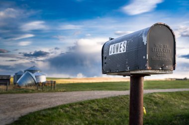 Rocky View County Alberta Canada, June 26 2022: The Jones rural mailbox for newspaper delivery at a farmyard entrance with grain silos blown over after a storm.