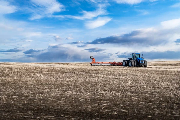 Rocky View County Alberta Kanada 'da kayan tepelerle dolu tarlada dramatik bulutlu bir gökyüzünün altında bir saban çeken sekiz tekerlekli bir traktör..