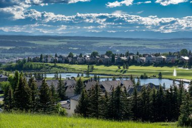 Cochrane Alberta Canada, July 14 2022: Overlooking a small Alberta town with the Glen Eagles Golf Course and distant Rocky Mountains. clipart
