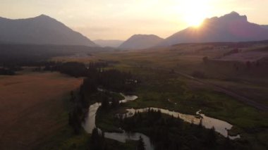 High aerial shot over the winding Crowsnest River with distant Canadian Rocky Mountains and train tracks in Alberta Canada at sunset.