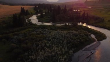 Aerial revealing shot over the winding Crowsnest River with distant Rocky Mountains in Alberta Canada at sunset.
