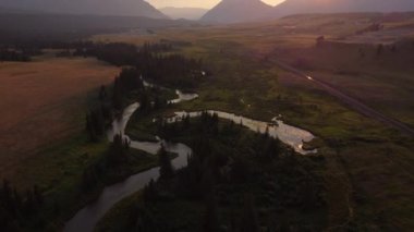 High aerial shot over the winding Crowsnest River with distant Canadian Rocky Mountains in Alberta Canada at sunset.