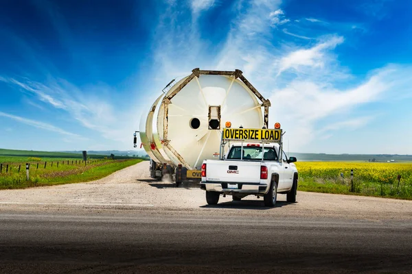 Kneehill County Alberta Canada, July 28 2022: An oversized load of grain silos carried on a semi trailer drives down a rural road with an escort vehicle.