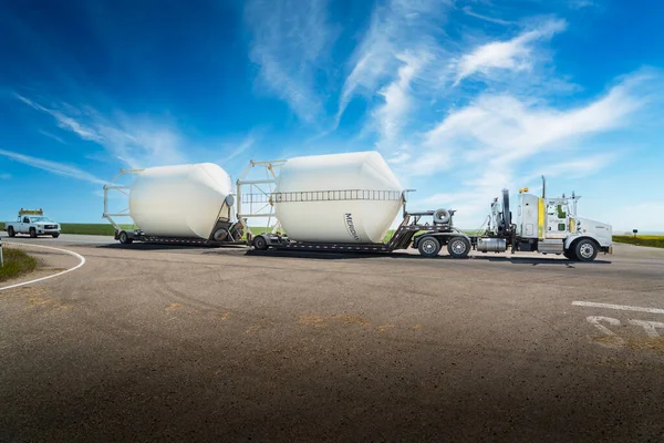 Kneehill County Alberta Canada, July 28 2022: An oversized load of grain silos carried on a semi trailer drives down a rural road with an escort vehicle.