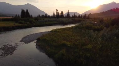 Low aerial over the Crowsnest River at sunset with distant Canadian Rocky Mountains in the Crowsnest Pass.