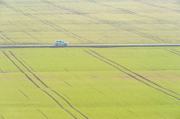 Car drives beside green fields