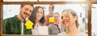 Yatay pankart ya da başlık Çok ırklı takım çalışmalarının penceresinden vurularak yapıştırma yapıştırmalarına gülen yüzlerle.