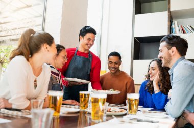 Lokantada gülen yüzlü bir grup genç arkadaş. Pizza servisi yapan Asyalı garson..
