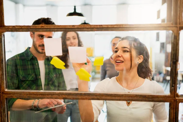Bir grup beyaz takım çalışanı pencere camındaki çıkartmalara bakarak fikirleri tartışıyor..