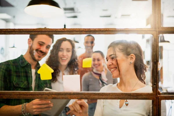 Gülümseyen genç bir bayan yeni bir strateji ya da iş arkadaşlarına planlar gösteriyor. Pencere camındaki yapıştırmaları kullanarak ekip çalışması yaparak pencereden ateş etmiş..