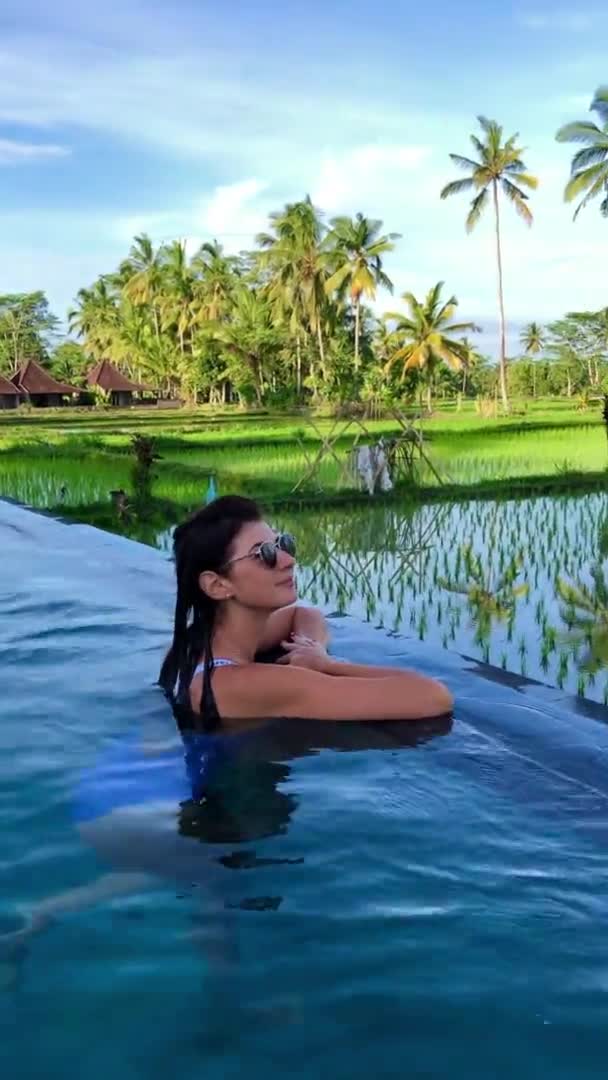 Красивые женщины отдыхают в бассейне с видом на рисовые террасы и пальмы на острове Бали.. — стоковое видео