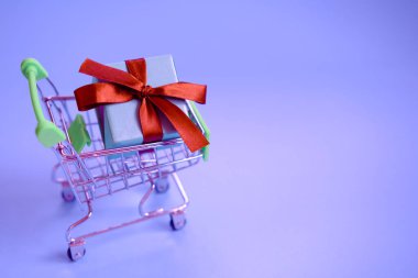 Alışveriş arabasında kurdeleli bir hediye kutusu. Konsept - hediye almak, internetten ve satıştan.