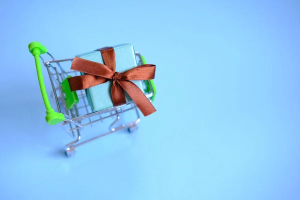 Una scatola regalo con un nastro nel carrello della spesa. Concetto - acquisto di un regalo, online e vendita. — Foto Stock
