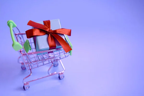 Una scatola regalo con un nastro nel carrello della spesa. Concetto - acquisto di un regalo, online e vendita. — Foto Stock