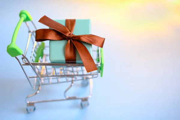 Una scatola regalo con un nastro nel carrello della spesa. Concetto - acquisto di un regalo, online e vendita. — Foto Stock