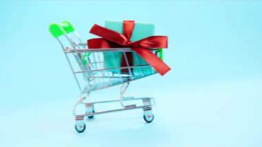 Alışveriş arabasında kırmızı kurdeleli 4K hediye kutusu. Konsept - hediye almak, internetten ve satıştan.