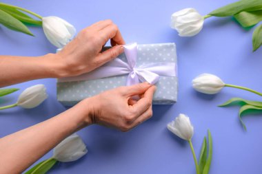  Kadınlar hediyeyi açar. Mavi ve çiçekli lalelerin hediye paketinde beyaz kurdeleyle gelen kız hediye kutusunu açar. Hediye paketi. Kapat. Üst görünüm.