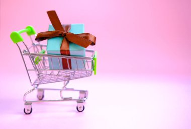 Alışveriş arabasında kurdeleli bir hediye kutusu. Konsept - hediye almak, internetten ve satıştan.