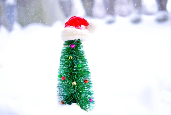 Uma árvore de Natal na neve decorada com um chapéu de Pai Natal na neve do lado de fora — Fotografia de Stock