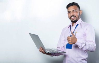 Elinde dizüstü bilgisayarı olan bir adam kameraya doğru başparmağını kaldırıyor.