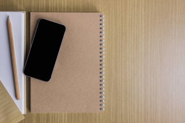 Ahşap masadaki cep telefonu ve not defterinin üst görüntüsü