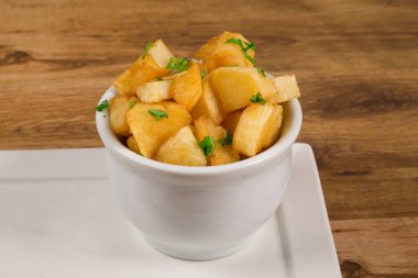 Fried potato cubes served in a white bowl on a wooden table.
