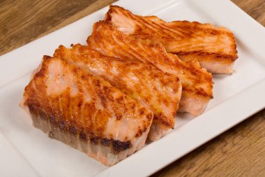 Grilled salmon fillet served on white plate on wooden background.