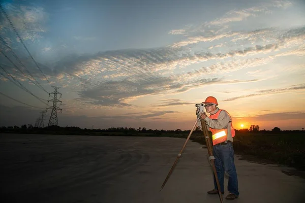 Theodolite Berendezéssel Dolgozó Mérnök Vagy Földmérő Nagyfeszültségű Háttérrel Rendelkezik Naplementekor Stock Kép