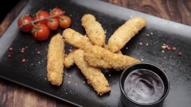 Tamamlanmış sulu tavuk tabakta güzelce yatıyor. Karanlık arka plan. Tavuk şeritleri tadıyor. fast food. Amerikan yemeği. Kızarmış, barbekü soslu tavuk şeritleri. Yavaş çekim