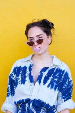 Kadın sarı arka planda sakız şişiriyor.