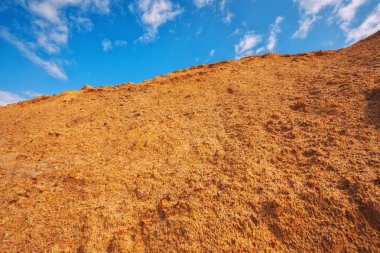 Büyük endüstriyel kum yığını. Mavi gökyüzüne karşı inşaat ve yol yapımında kullanıma hazır.