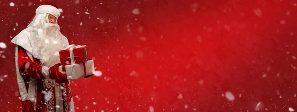 俄罗斯圣诞老人 莫罗兹饰 在一家红色咖啡馆里 白色礼品盒上绑着一条红色缎带 背景是喜庆的红色 上面挂满了雪花 带有复制空间的全景横幅 — 图库照片